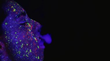 Ultraviyole boyayla makyaj yapmış güzel bir genç kız sigara içiyor. Ağzından duman halkaları çıkıyor. Kutsal renklerin bayramı. Parlak, renkli, neşeli boyama kitabı