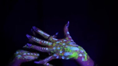 A hand with a fluorescent ethnic pattern shows the movement of the hands. Fluorescent paint, body art concept. Glows in the dark. Gestures, symbols, hand movements