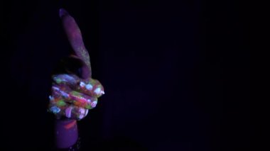 A hand with a fluorescent ethnic pattern points its finger at the viewer. Fluorescent paint, body art concept. Glows in the dark. Gestures, symbols, hand movements