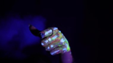 A hand with a fluorescent ethnic pattern points its finger at the viewer. Fluorescent paint, body art concept. Glows in the dark. Gestures, symbols, hand movements