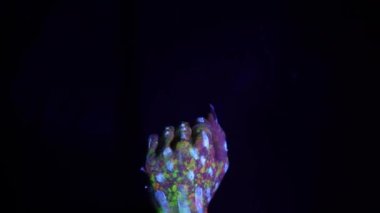A hand with a fluorescent ethnic pattern shows the middle finger. Fluorescent paint, body art concept. Glows in the dark. Gestures, symbols, hand movements