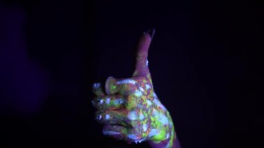 A hand with a fluorescent ethnic pattern shows a thumbs up. Fluorescent paint, body art concept. Glows in the dark. Gestures, symbols, hand movements