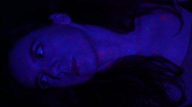 Neon ışıklı model kadın, floresan makyajlı güzel model kız, UV ışığında dans eden disko dansçısının sanat tasarımı, renkli makyaj. Gece kulübü, parti. 4K video