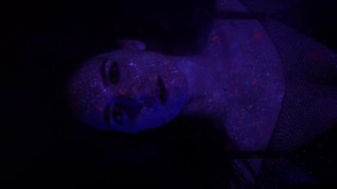 Neon ışıklı model kadın, floresan makyajlı güzel model kız, UV ışığında dans eden disko dansçısının sanat tasarımı, renkli makyaj. Gece kulübü, parti. 4K video