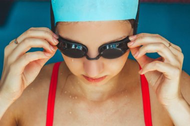 Extreme close-up shot of a Caucasian girl head with a swimming cap and hands putting swimming goggles, preparing for training in the pool