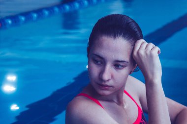 Young beautiful brunette girl on the background of the pool. Portrait of a girl near the side of the pool. Swimming, healthy lifestyle