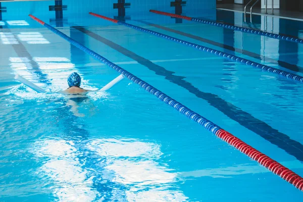 Happy muscular swimming woman in goggles and cap in the pool and represents the concept of health and good shape. Beautiful female model in the water doing synchronized swimming