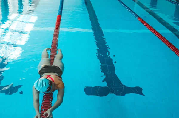 Happy muscular swimming woman in goggles and cap in the pool and represents the concept of health and good shape. Beautiful female model in the water doing synchronized swimming