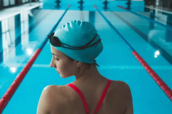 Happy muscular swimming woman in goggles and cap in the pool and represents the concept of health and good shape. Beautiful female model in the water doing synchronized swimming