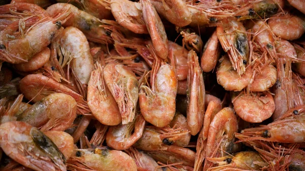 Pink fresh frozen shrimps with ice in a supermarket or fish shop. Uncooked seafood close up background. Fresh frozen prawns, delicacies, sea food concept, close up
