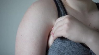 Kolları sarkık, açık tenli genç bir kadın. Üzgün, kötü vücutlu kız. Kollarında yağ var, kasları şişmemiş, derisi sarkık. 4k video. Şişman, şişman kolları var.