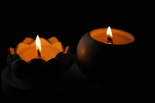 A set of lit white candles flickering in the dark on a black background with one candle in focus in the foreground. Lighting a candle. A burning candle. Beautiful handmade candles. Cozy atmosphere in the house