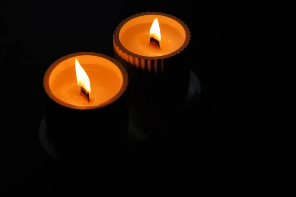 A set of lit white candles flickering in the dark on a black background with one candle in focus in the foreground. Lighting a candle. A burning candle. Beautiful handmade candles. Cozy atmosphere in the house