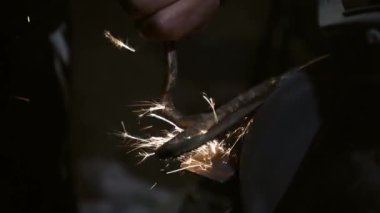 Erkek eli makinede çalışır. Sıcak metalden kıvılcımlar çıkıyor. Adam çelik üzerinde çok çalıştı. Elektrik öğütücüsünde bileme makinesi, döner taşta elle keskinleştirme, yakın plan.