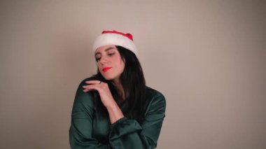 Noel Baba şapkalı genç pozitif kız gri arka planda izole edilmiş. Noel Baba şapkalı mutlu genç kadın dans ediyor. İnsan kavramı ve kış tatili
