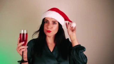 Elinde bir bardak şampanyayla, kırmızı şapkalı, uzun saçlı genç bir kız. Yeni yıl arifesinde güzel elbiseli bir kız dans eder. Noel reklamı. Kış tatili