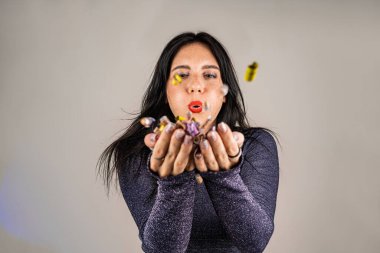 Neşeli, güzel esmer kız ellerinden konfeti üflüyor. Tatilin kutlaması. Şenlikli yeni yıl atmosferi. Eğlenceli bir etkinlik. Noel konsepti