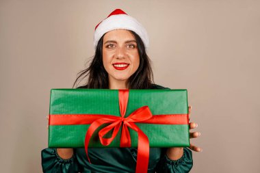 Noel Baba şapkalı, yeşil elbiseli ve elinde hediye kutusuyla mutlu ve mutlu bir kızın stüdyo fotoğrafı. Mutlu noeller. Yeni yıl kavramı