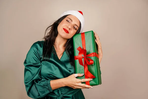 stock image Studio shot of beautiful happy joyful excited girl in santa hat and green dress holding gift box in hand. Merry Christmas. New year concept