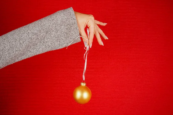 Kırmızı arka planda izole edilmiş kırmızı yuvarlak Noel ağacı topu. Bir kadının eli dekoratif bir Noel ağacı oyuncağı tutuyor. Yeni yıl ve Noel konsepti. Tatil, Noel ağacı ve evi süslemek.