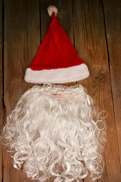 Santa hat and beard on a wooden background. Symbolism of New Year\'s holidays. Christmas and new year concept. Change of clothes, change of image
