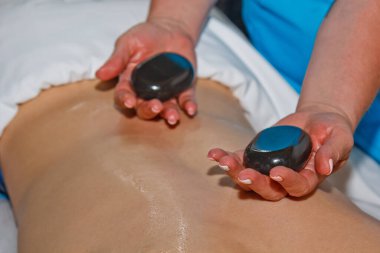 Sağlık konsepti. Lüks bir kaplıca ve sağlık merkezinde geleneksel sıcak taş masajının canlandırıcı etkisi altında rahatlatıcı genç bir adam. İşten sonra iyileşme