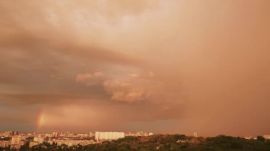 Evlerin üzerinde gökkuşağı olan fırtına bulutları. Gökyüzü turuncu bulutlarla kaplıdır. Şehir manzarası