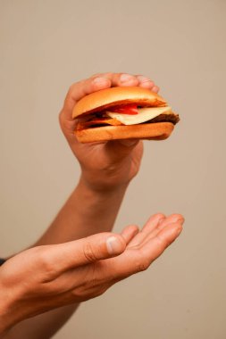 Ahşap masada ev yapımı sığır burger tutan eller. Lezzetli fast food hamburgeri yemeye hazır. Sağlıksız gıda konsepti. Adam hamburgeri elleriyle tutuyor. Eve teslim. Burger yiyen delikanlıyı yakından çek.