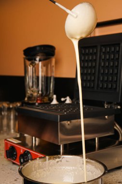 Yemek hazırlama. Belçika Waffle 'ı yapıyorum. Kadın eli evdeki mutfakta waffle makinesine hamur döker. Kahvaltıda. Belçika waffle 'ı hazırlamak için sıvı hamurlu waffle makinesi. Yemek pişirme süreci