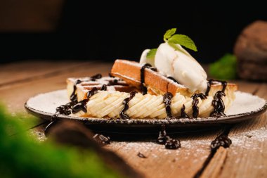 Üstünde muz, dondurma ve çikolata olan Belçika waffleları. Dondurma ile servis edilir. Tatlı gözlemeler. Çay saati için lezzetli bir tatlı. Tatlının üstüne nane şekeri. Yemek pişirme süreci