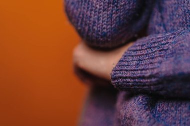 Mor örgü kazaklı bir kadın elini dirseğinin altına koydu, yüzünü göstermeden, yakın çekim. Yakınlık ve belirsizlik belirtisi. Sözsüz işaret dili, yatay resim