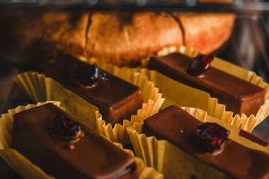 İçinde çeşitli kek ve kekler olan bir vitrin. Üstünde kiraz olan çikolatalı çörekler. Pastalar arka arkaya düzenlenir, bazıları çikolatadır.