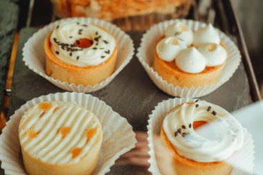 İçinde çeşitli kek, kek ve çörekler olan bir kutu göster. Mangolu tartlar ve aptal peynirli turtalar siyah tabakta sıralanır..