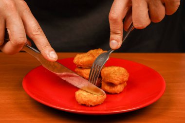 Obezite. Amerikan yemeği. Çatal ve bıçakla yemek. Tavuk nugget yiyen adam. Tavuk külçeleri tabakta. Ketçaplı tavuk nugget. Fast food. Abur cubur. Sağlıksız bir yaşam tarzı. Kaloriler