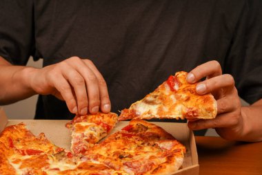 Pizzayı elimle alıyorum, manzarayı kapatıyorum. Pizzacıda lezzetli yemekler. Paket servis kavramı. Fast food siparişi. Restoran reklamı. Lezzetli peynirli pizza. - Pizza. Sağlıksız yiyecekler. Abur cubur. Yağlı yemek.