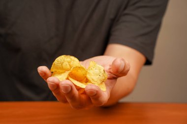 Patates cipsi yiyen adam. Patates cipsi yığınını tutan bir elin görüntüsü. Elleri patates cipsi tutuyor. Fast food. Abur cubur. Sağlıksız bir yaşam tarzı. Kalori. Obezite. Amerikan yemekleri.