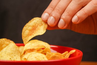 Ellerinde patates cipsi var. Patates cipslerini kaseden çıkaran bir el görüntüsü. Fast food. Abur cubur. Sağlıksız bir yaşam tarzı. Kalori. Obezite. Amerikan yemeği. Patates cipsi yiyen adam.