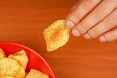 Fast food. Abur cubur. Sağlıksız bir yaşam tarzı. Kalori. Obezite. Amerikan yemeği. Patates cipslerini kaseden çıkaran bir el görüntüsü. Ellerinde patates cipsi var. Patates cipsi yiyen adam.