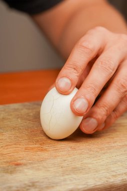 Tahta üzerinde tavuk yumurtası tutan adam. Haşlanmış yumurta. Kabuklarından yumurta temizleme, kapat. Sağlıklı yiyecekler. Protein. Sporcu yemeği. Yemek hazırlıyorum. Dikey fotoğraf. Vejetaryen.