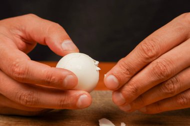 Healthy food. Protein. Man holding chicken egg over wooden board. Boiled egg. Cleaning egg from shelling, close up. Sportsmens food. Preparing food. Horizontal photo. Vegetarian clipart