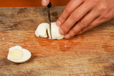 Yemek hazırlıyorum. Yatay fotoğraf. Masada haşlanmış tavuk yumurtası var, yakın plan. Sağlıklı yiyecekler. Protein. Sporcu yemeği. Vejetaryen. Mans eller tahta bir tahta üzerinde bir bıçakla tavuk yumurtası kesti.
