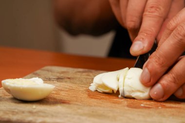 Mans eller tahta bir tahta üzerinde bir bıçakla tavuk yumurtası kesti. Yatay fotoğraf. Masada haşlanmış tavuk yumurtası var, yakın plan. Yemek hazırlıyorum. Sağlıklı yiyecekler. Protein. Sporcu yemeği. Vejetaryen