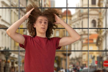 Kıvırcık saçlarından parçalar tutan bir adam. Erkek saç bakım konsepti. Genç Avrupalı adam uzun kıvırcık saçlarını elleriyle tarıyor. El sallayan saçlarını önemsiyor ve şekillendiriyor. Stüdyonun arka planında duruyorum.