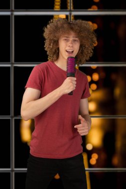 Genç Avrupalı bir adam, mikrofon olarak kendine güvenen, güzel bir arka planda izole edilmiş bir şarkı söyleyen. Çalı çırpı şarkı söylüyor