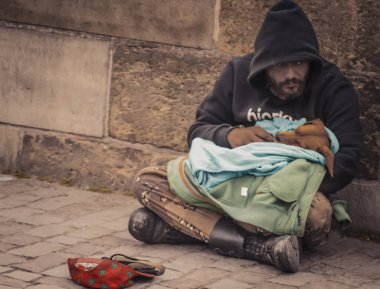 Prague, Czech Republic - May 11, 2019: A homeless man sitting on the street and holding his dog in hands with cap for begging money near him. A broken man living on street. Life of homeless people clipart