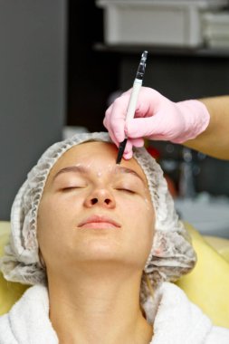 Yüzünde estetik ameliyat talimatları olan çekici bir hasta. Cerrah bir insanın yüzüne dokunuyor. Estetik kozmetoloji ve enjeksiyon kavramı