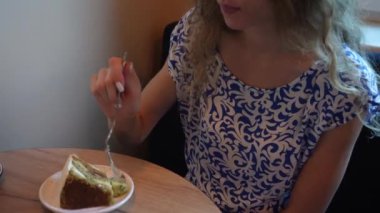 Mavi ve beyaz elbiseli bir kadın ahşap bir masada oturur, sıcak bir ortamda kahvesini yudumlayarak bir dilim pastanın tadını çıkarır, yemeğini yemeye hazırdır.