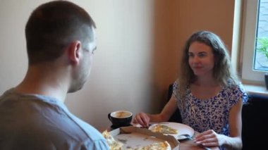 İki arkadaş ya da bir çift küçük bir kafede kahve ve pizza paylaşıyor. İyi yemek ve sohbetle dolu sıradan yemek anı, sıcak ve davetkar bir birliktelik ve zevk sahnesi yaratır.