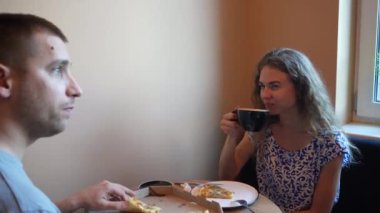 İki arkadaş ya da bir çift küçük bir kafede kahve ve pizza paylaşıyor. İyi yemek ve sohbetle dolu sıradan yemek anı, sıcak ve davetkar bir birliktelik ve zevk sahnesi yaratır.