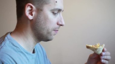 Evde otururken pizza yiyen genç bir adam servis içkisiyle. Bir adam teras masasında oturmuş, bir dilim pizza ve soğuk içeceğin tadını çıkarıyor.